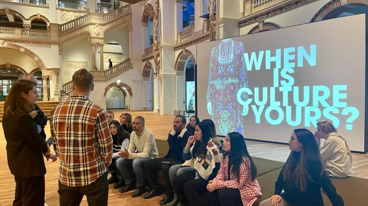 a grou of people sitting in a museum with a screen behind them that says when is culture yours?